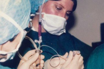 A female medic wearing scrubs, a cap and mask, at work at the clinic. The photograph dates from the early 1980s.