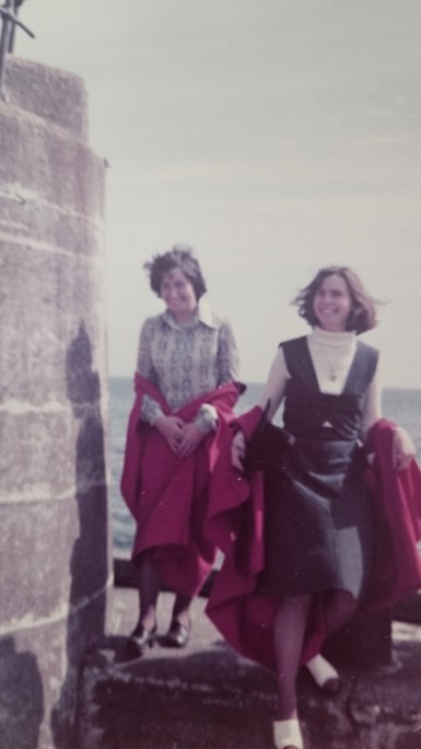 Anne and Jenny walking side by side smiling, wearing their red gowns off the shoulder.