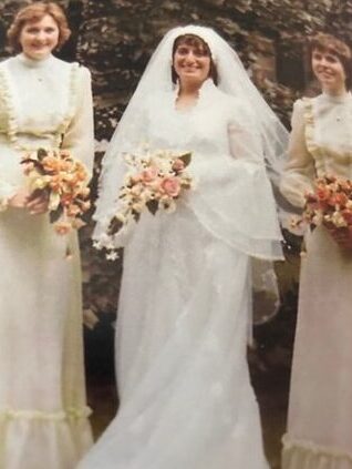 Jenny is in the centre wearing a white wedding dress and veil, her two bridesmaids stand either side of her smiling.