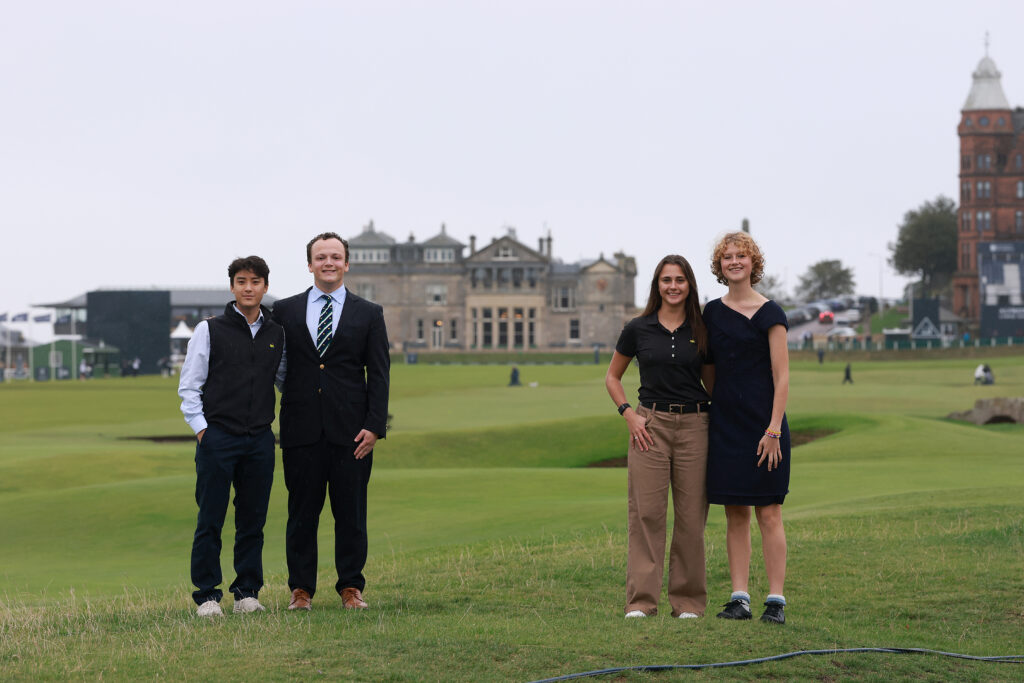 Four students, two male, two female, in formal wear standing on the Old Course golf course with the Royal & Ancient Golf Club in the background.