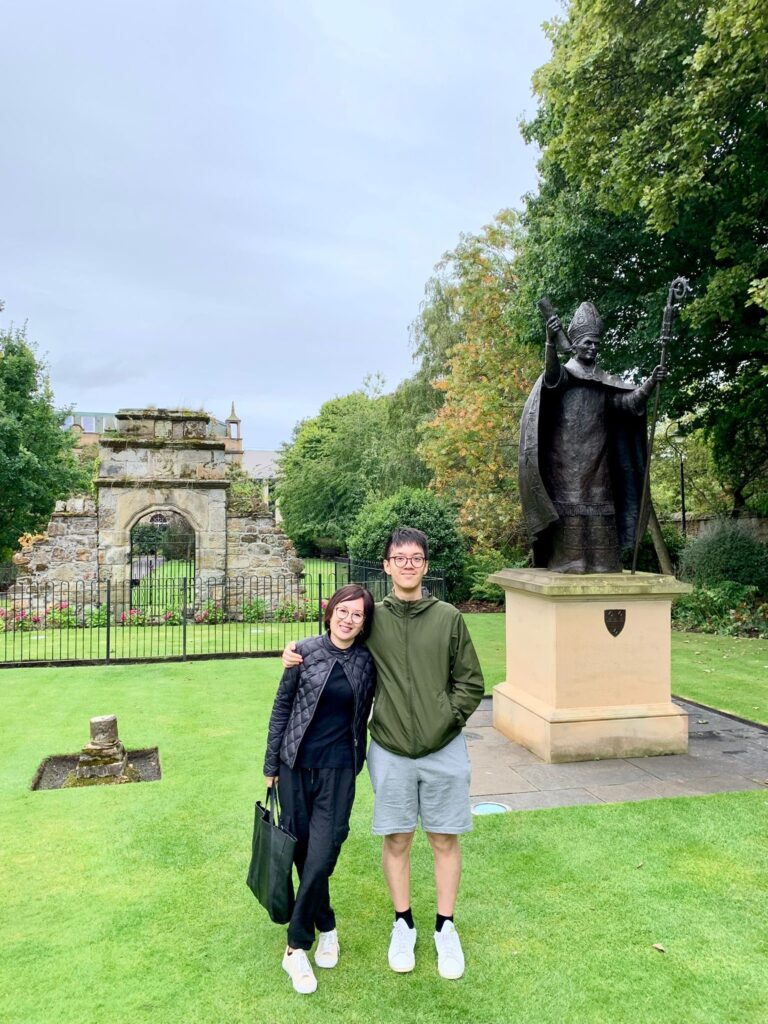 Helena and her son stand smiling in St Marys Quad, St Andrews. The Bishop Wardlaw statue can be seen to the right of the pair.