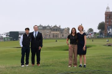 Four students, two male, two female, in formal wear standing on the Old Course golf course with the Royal & Ancient Golf Club in the background.