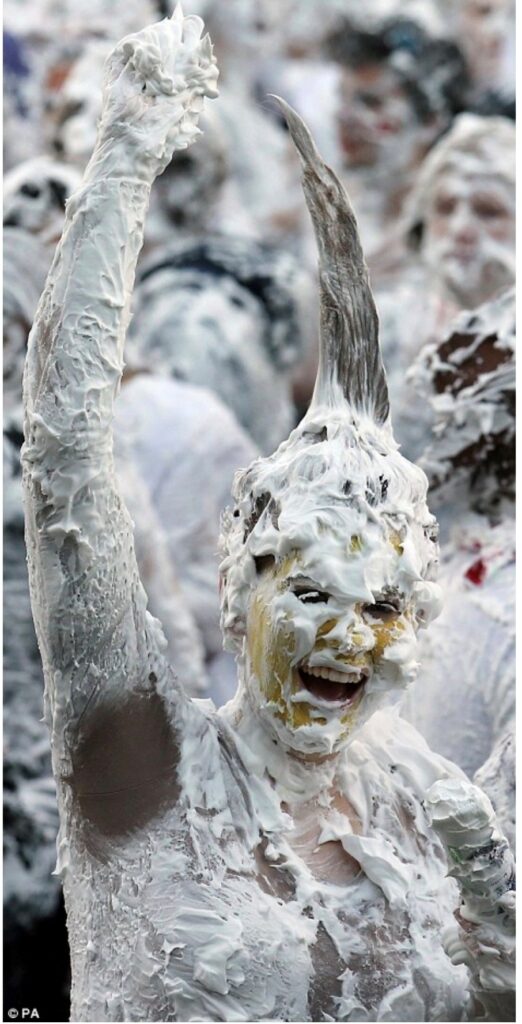 Jessica smiles at the camera, covered in foam, with her hand triumphantly in the air. Her hair stands on end covered in foam. 