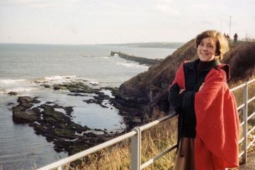Christina stands smiling in her red gown, the sea and the historic St Andrews pier can be seen in the background.
