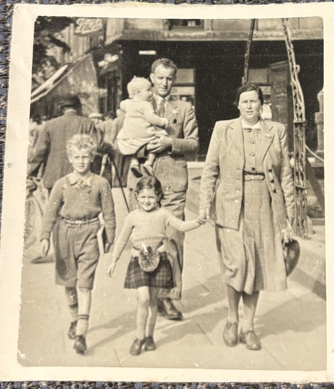 A black and white archive photograph showing a family of five walking down the street