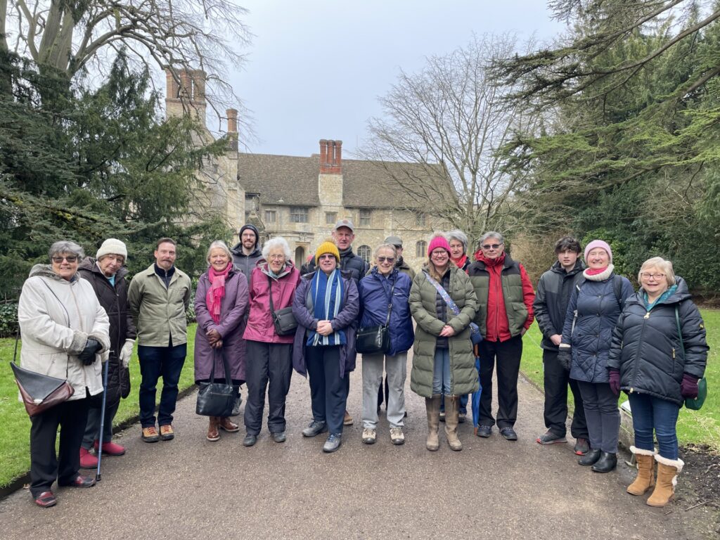 16 members of the club, dressed in outdoor clothing, pose for a group photo outside Anglesey Abbey