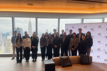 Group of students stand smiling in front of EY branding and New York City skyline