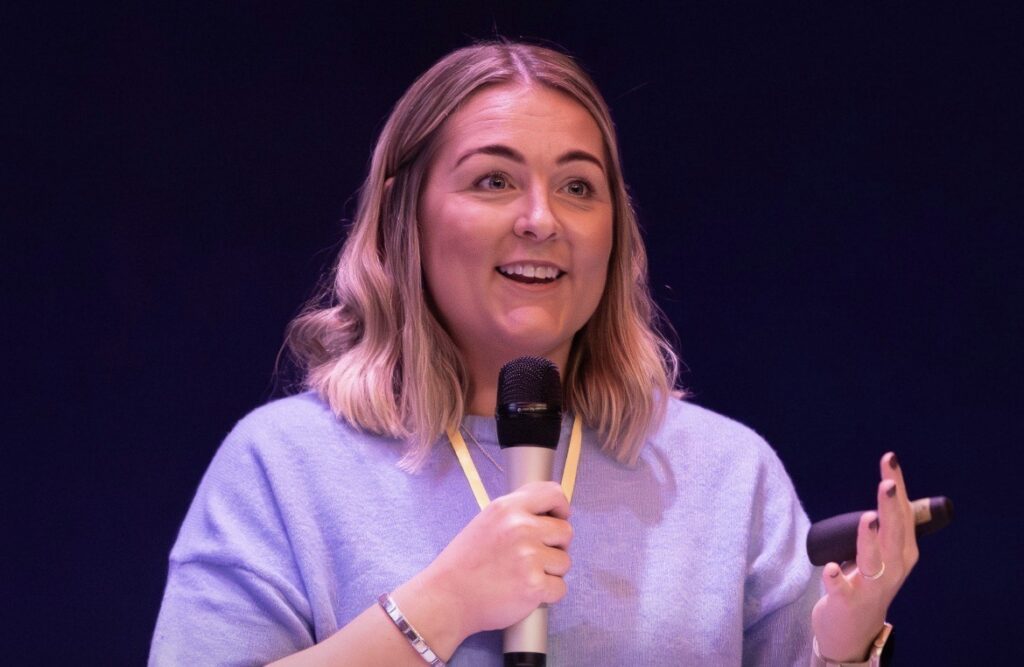 Collette is pictured at a public speaking event, holding a microphone