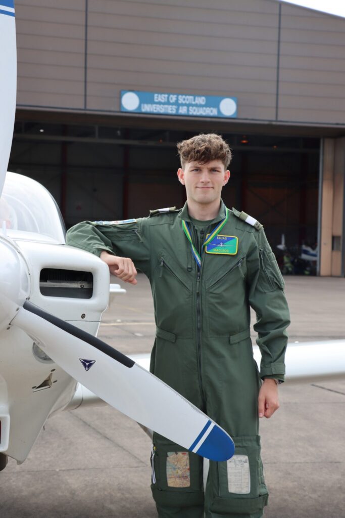 Luke poses for a photo, leaning on the side of a small plane, in his University of St Andrews Air Squadron uniform 
