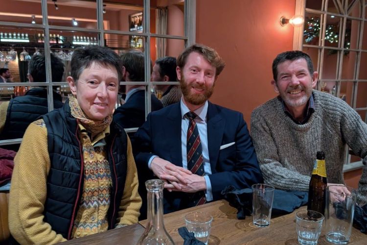 Three people are seated at a restaurant table with glasses and drinks.