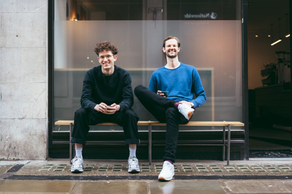 Ted and Max pose smiling for a photo on a bench outside a Redemption Roasters coffee shop location