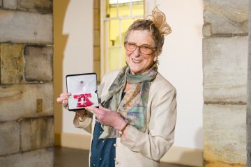 Bridget smiles at the camera, she is proudly holding her MBE.