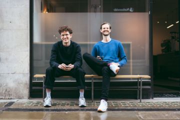 Ted and Max pose smiling for a photo on a bench outside a Redemption Roasters coffee shop location
