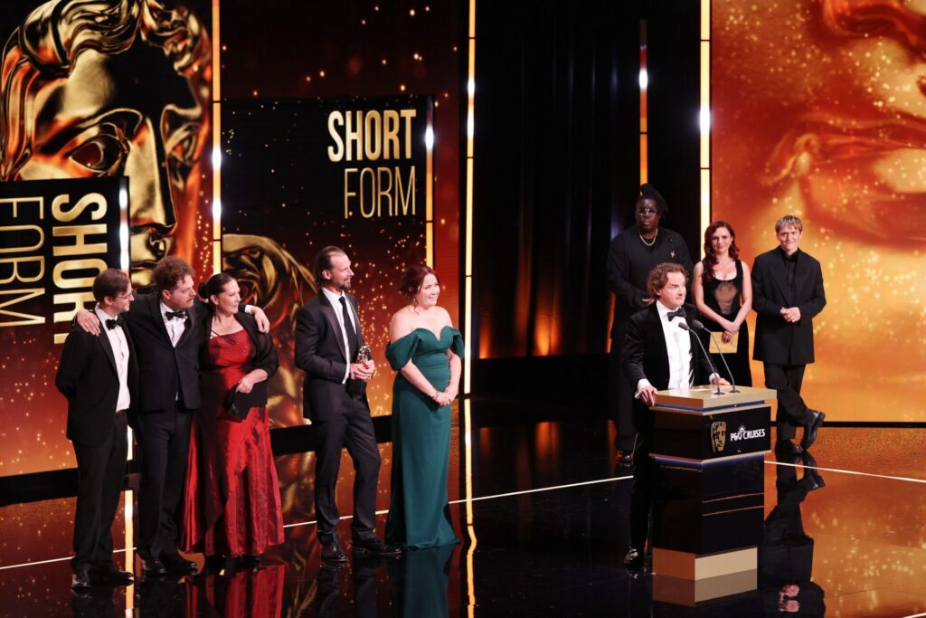 Jonny stands on stage at the 2026 BAFTAs, behind him are the JustSo team 