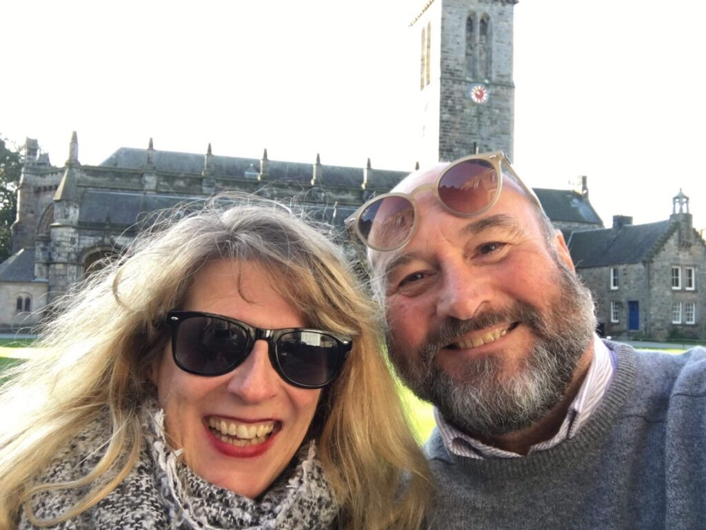 A couple smiling towards the camera wearing sunglasses.