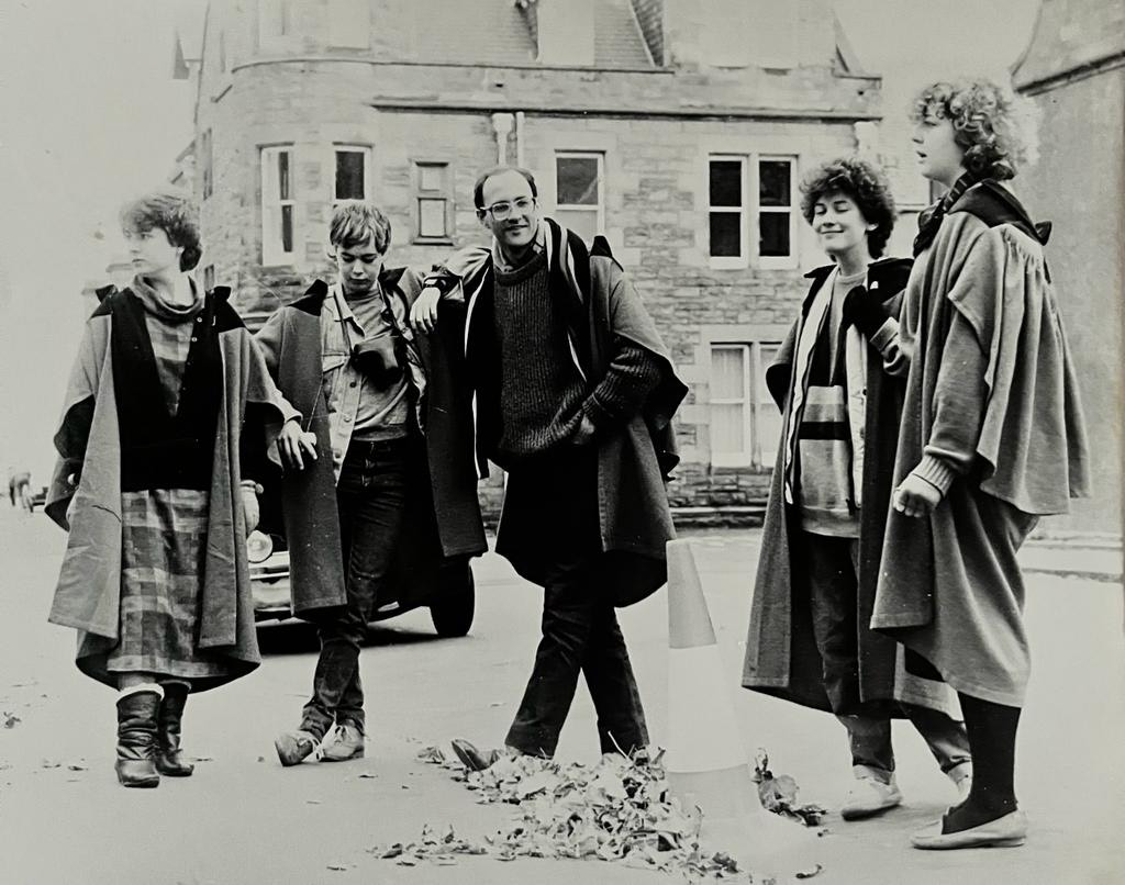 John Wallace, centre, pictured in a group of five students in University of St Andrews gowns in the 1980s. This is a black and white photograph.