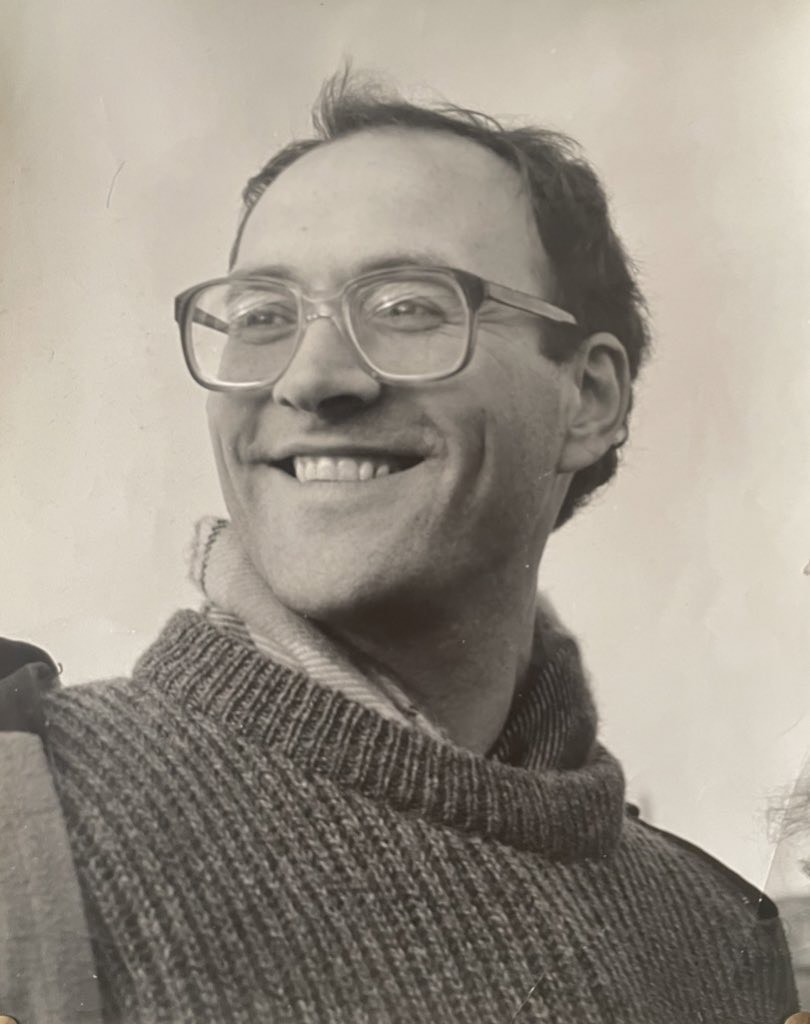 A black and white photograph of a man wearing spectacles and a knitted jumper