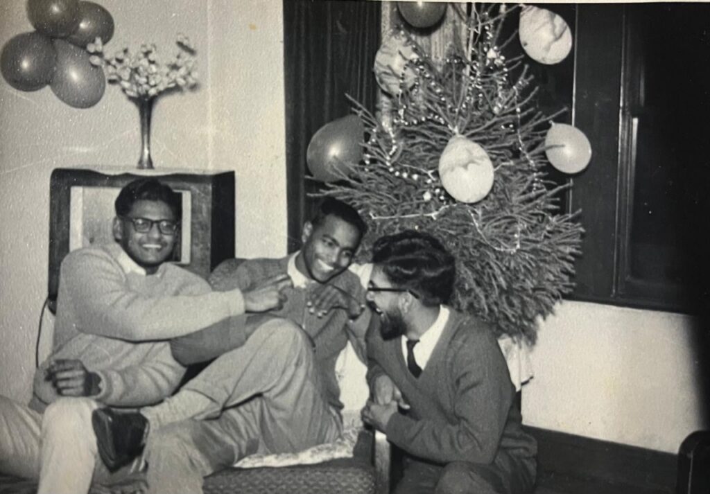 A black and white photograph from the early 1960s showing three male University of St Andrews students smiling, laughing, celebrating in front of a decorated Christmas tree.