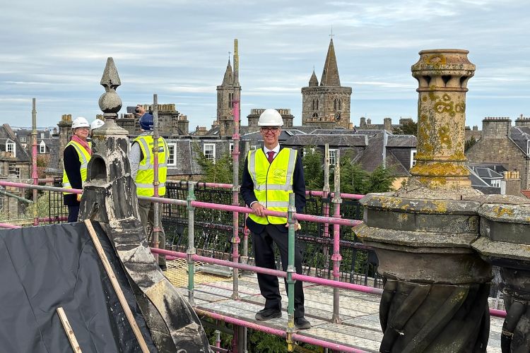 Richard Arnholt is pictured centre standing atop scaffolding on a historic St Andrews building. The town's skyline is visible in the background.